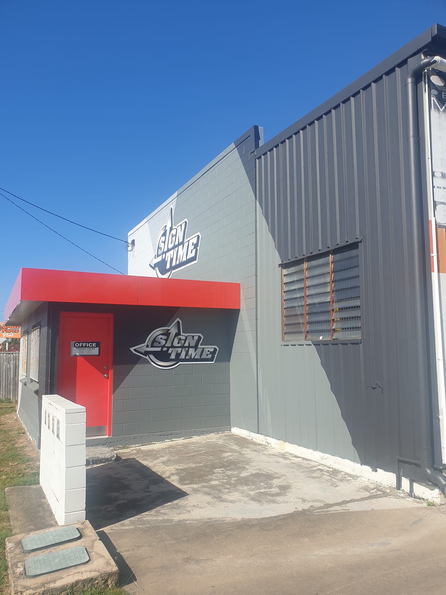 A gray building with a red door and a sign on it
