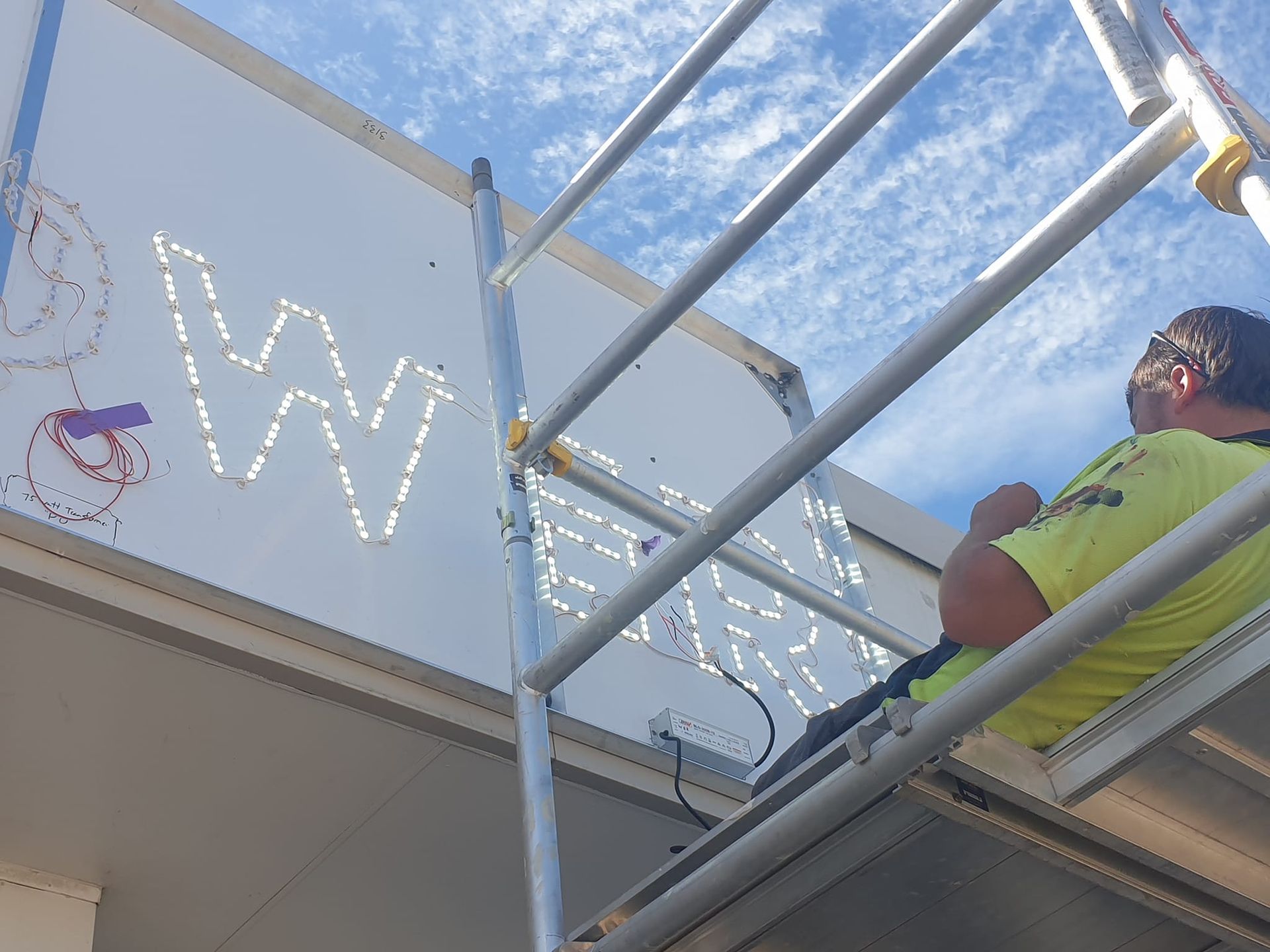 A man is standing on a scaffolding working on a sign.