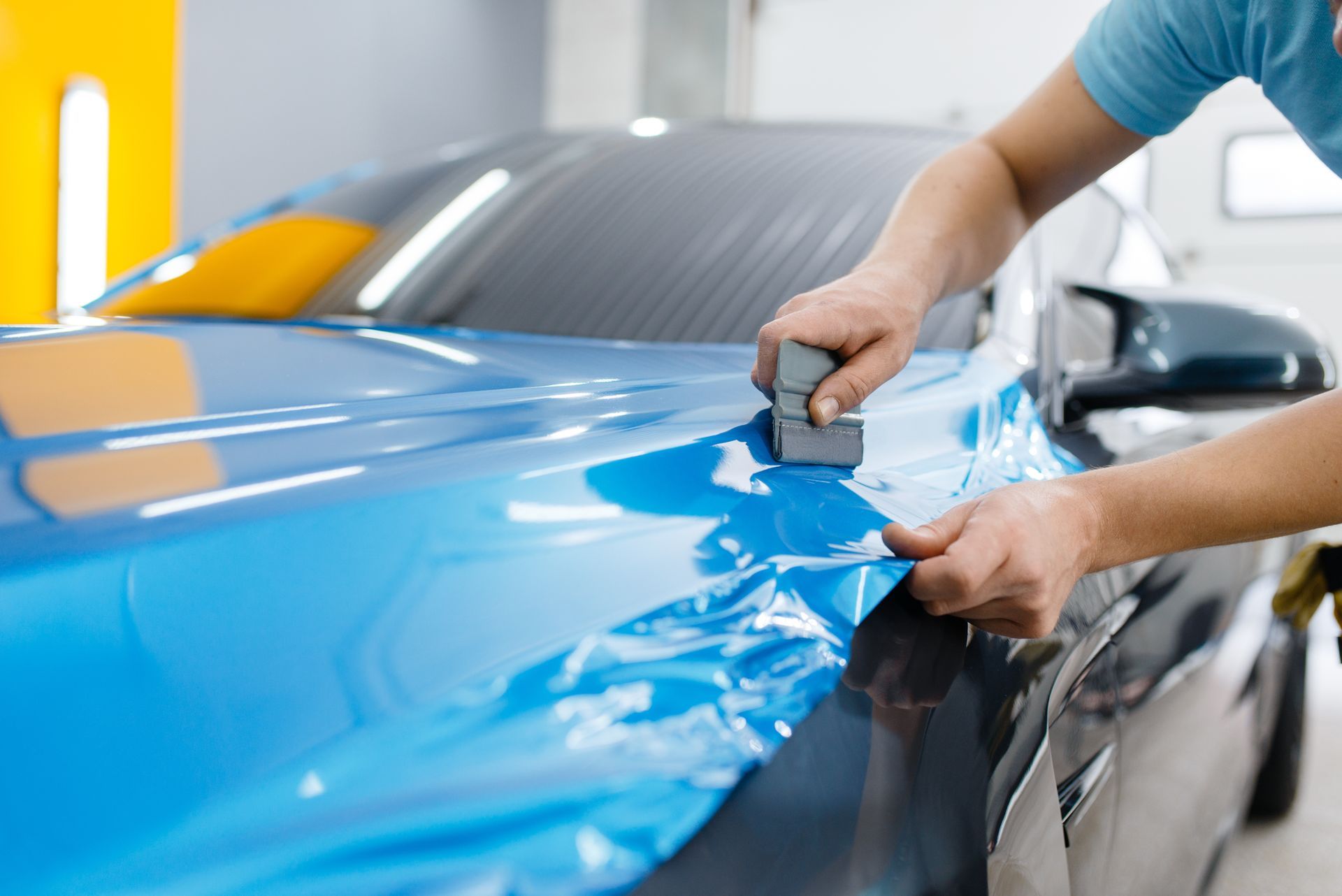 Close-up of a mechanic performing a blue car wrapping.