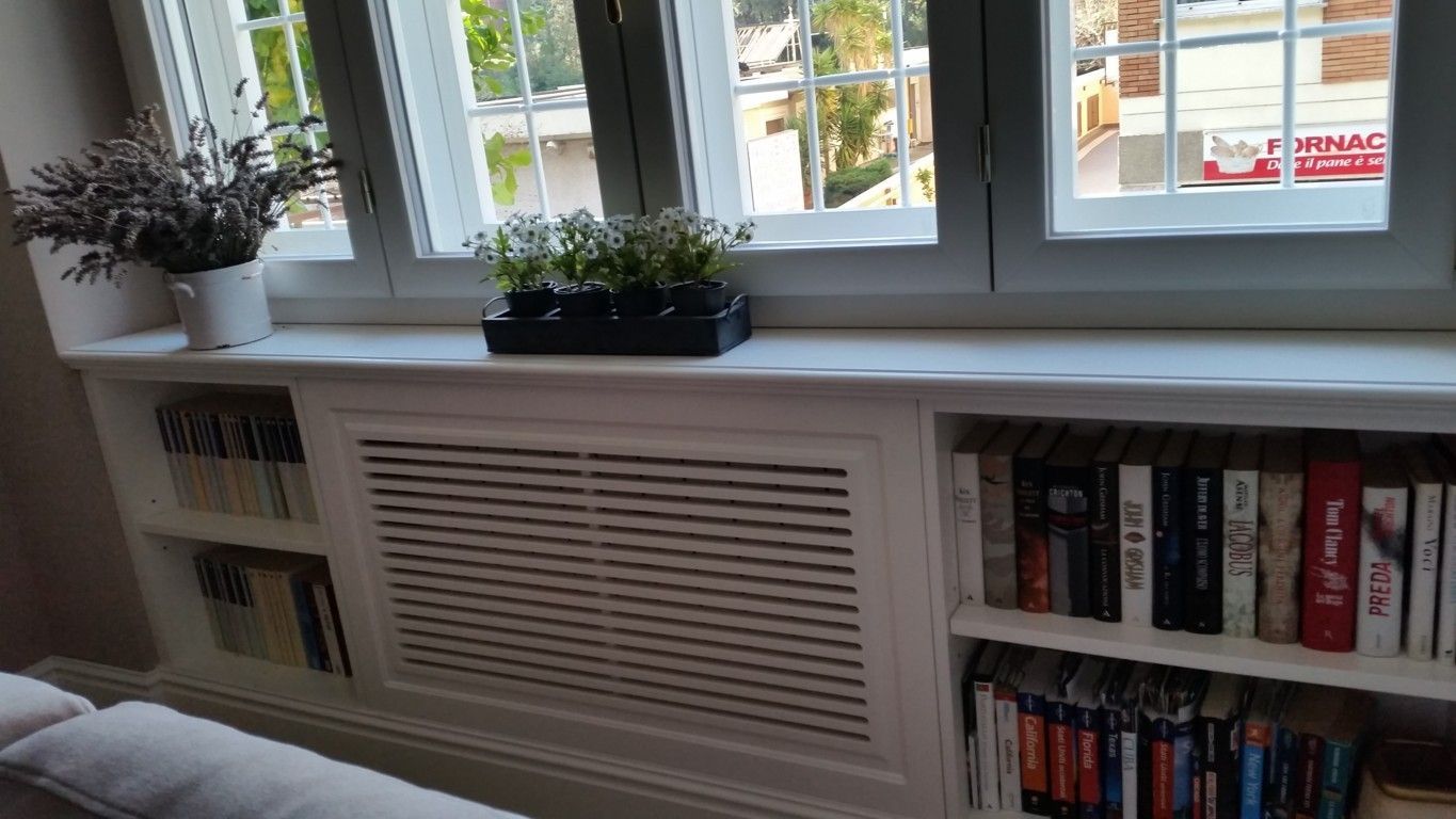 Davanzale con piante in vaso sopra un copritermosifone bianco e una libreria accanto alla finestra