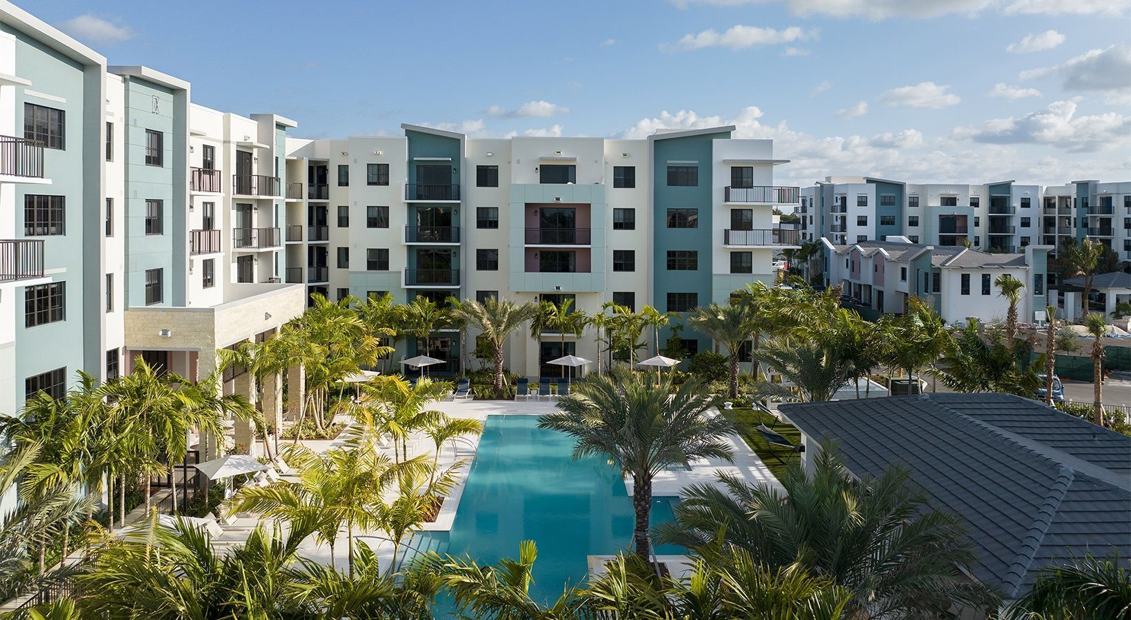 Modern apartment complex with a blue pool and palm trees under a clear sky