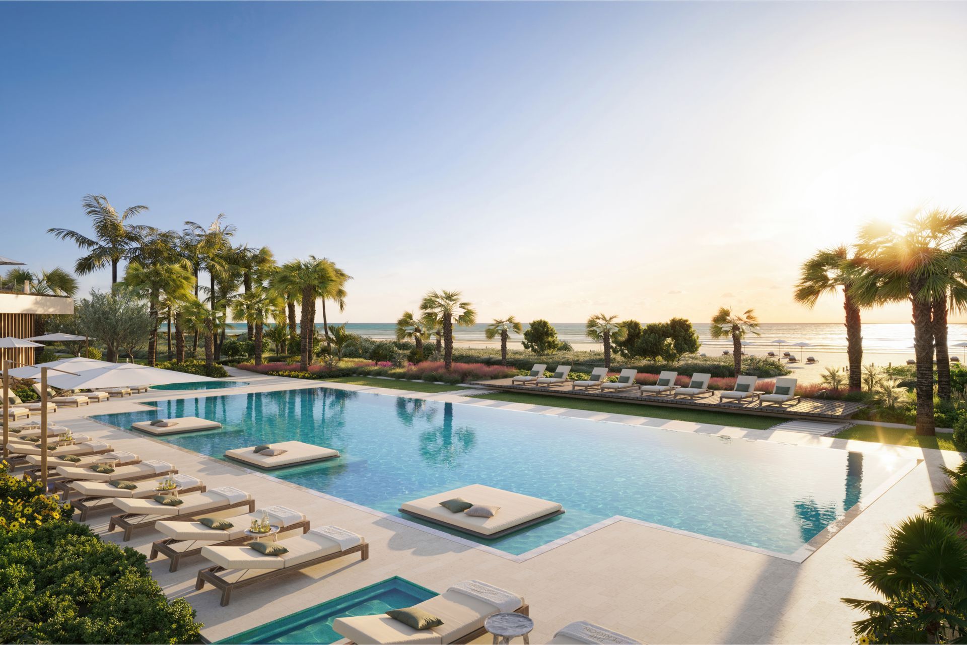 Luxury resort pool with lounge chairs, palm trees, and ocean view at sunset
