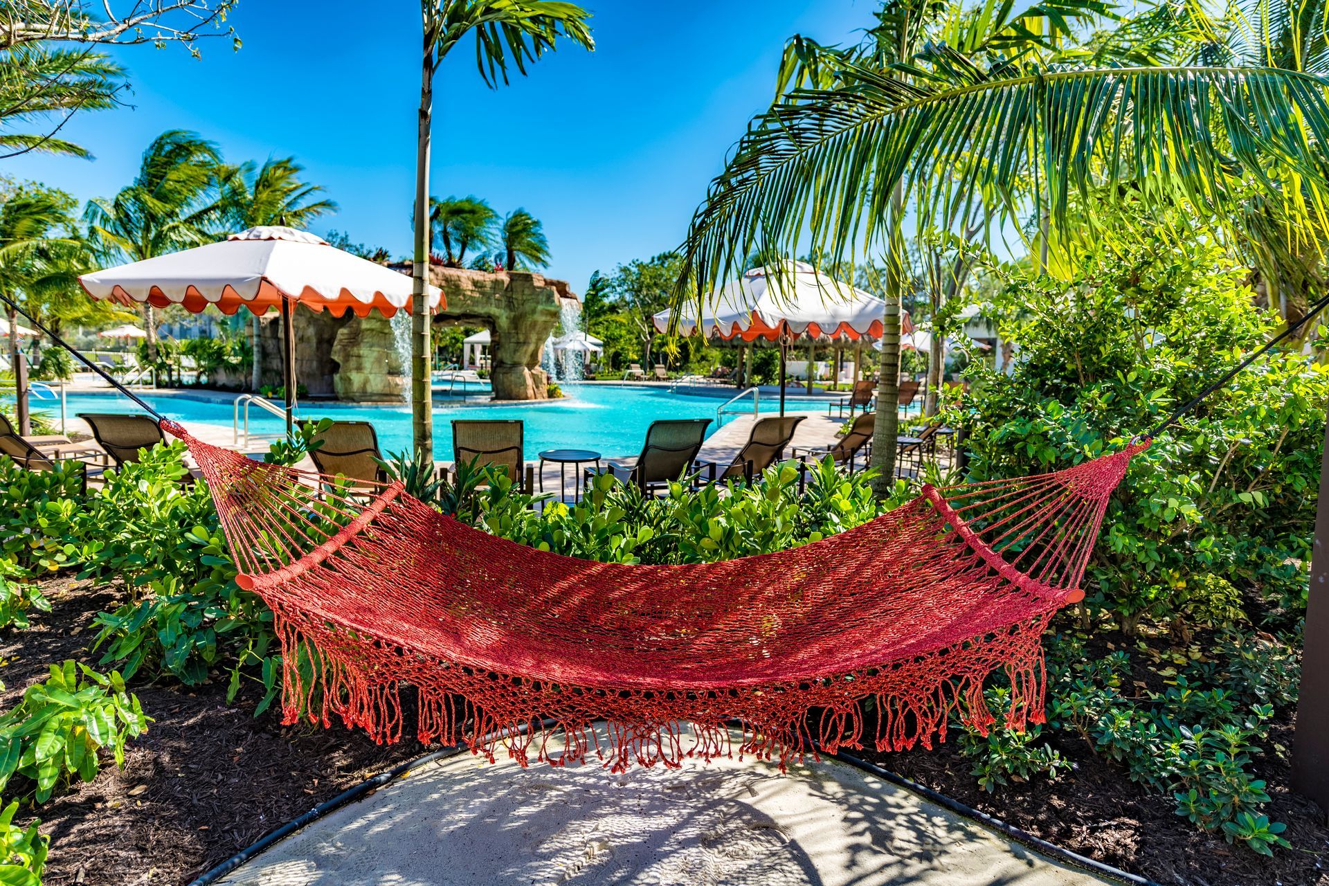 Red hammock in a tropical garden beside a resort pool with palm trees and umbrellas