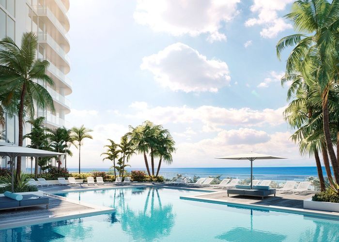 Luxury beachfront pool with palm trees, lounge chairs, and ocean view under a bright blue sky