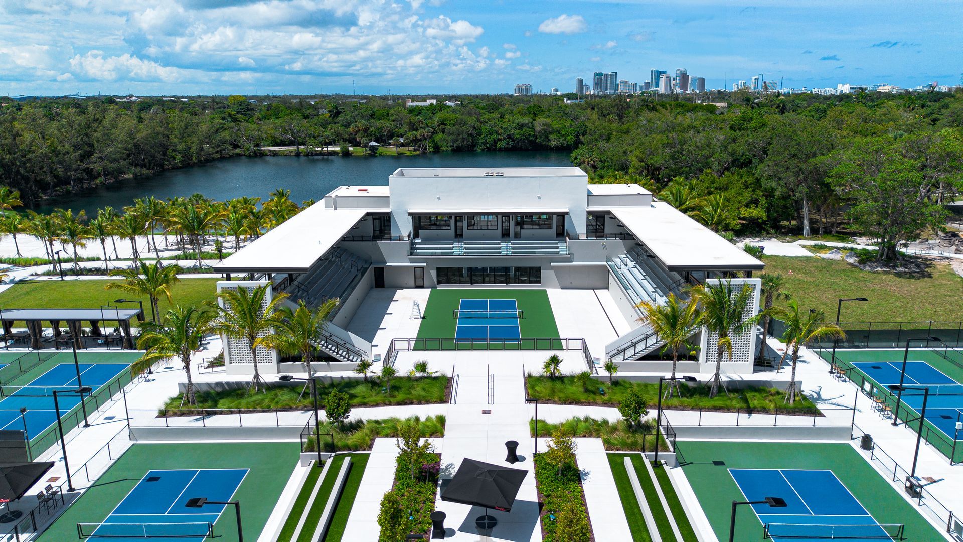 Resort-style outdoor pool with turquoise water, lounge chairs, palm trees, and a modern building under a blue sky