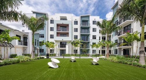 Modern apartment courtyard with green lawn, white buildings, palm trees, and outdoor seating
