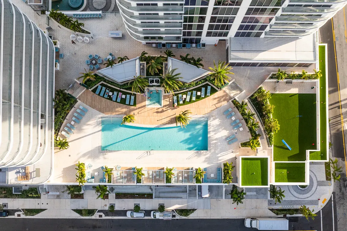 Aerial view of a modern apartment courtyard with a turquoise pool, lounge areas, and green lawns