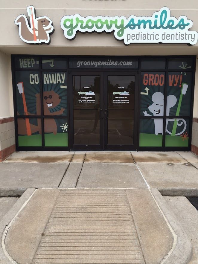 Exterior of Groovy Smiles pediatric dentistry, with cartoon animals and text on windows, and a squirrel logo.
