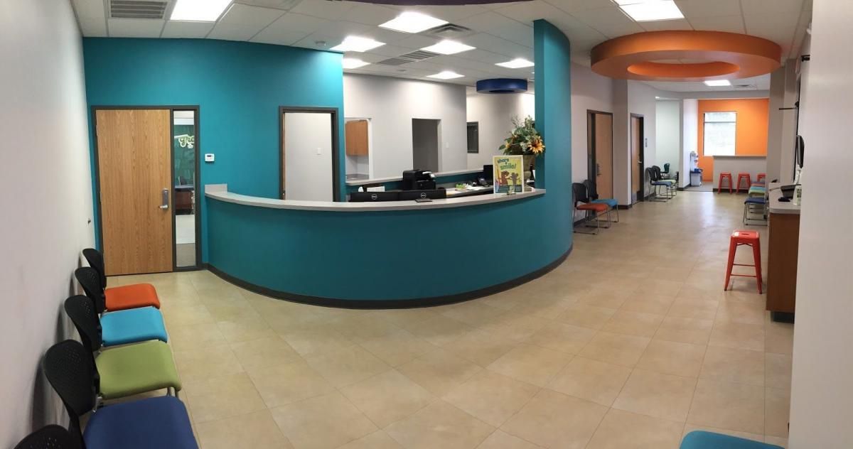 Reception area of a medical office with teal walls, a curved front desk, and a waiting area with colorful chairs.