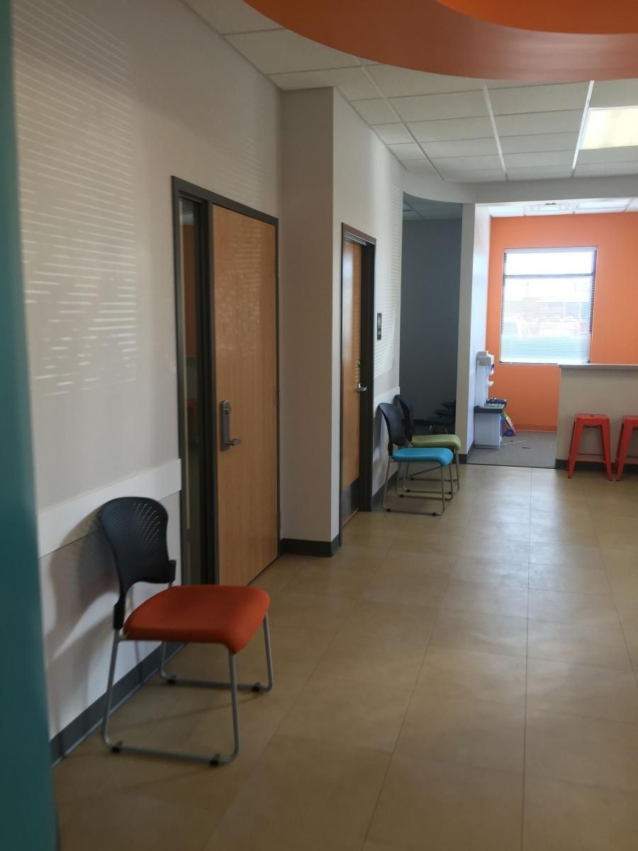 Hallway with chairs, two doors, and a window in an office setting. Orange and turquoise accents.