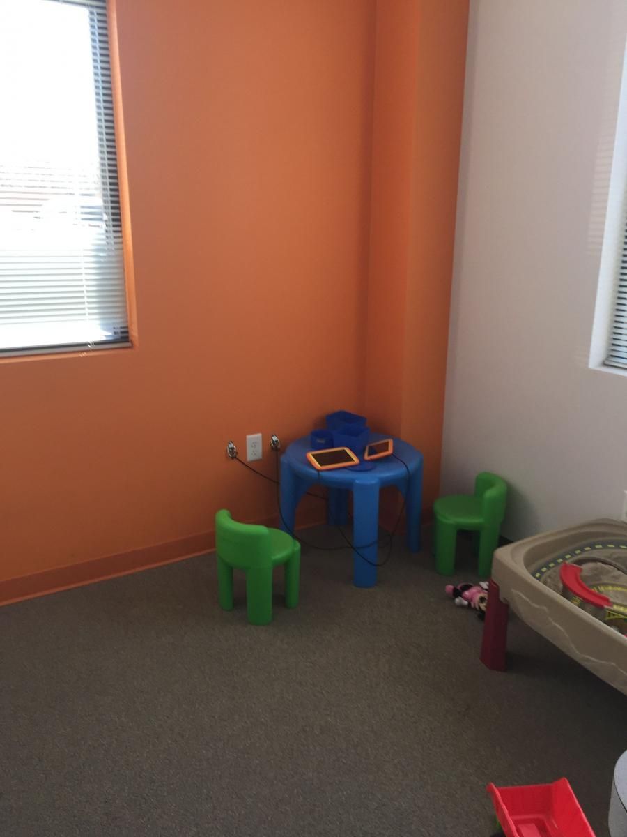 Play area: orange and beige walls, blue table, green chairs, and toy water table.