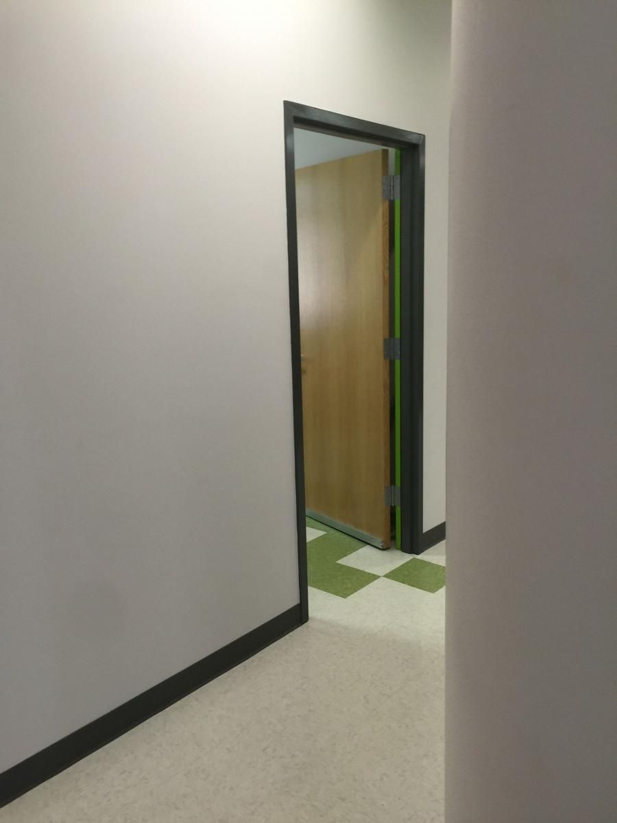 Hallway with a doorway leading to a room with a closed wooden door and checkered green and white floor.