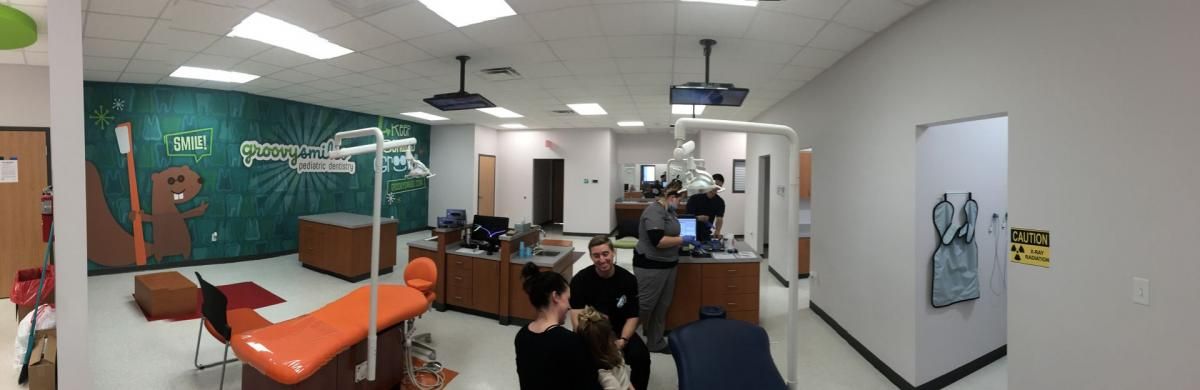 Interior of a dental office with an orange chair and people sitting and standing. Green mural on wall.