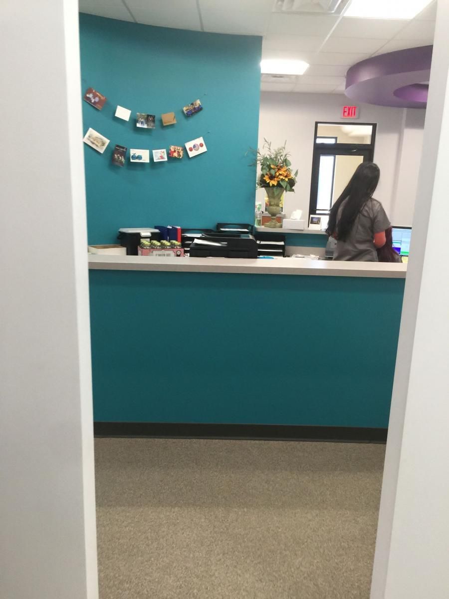 Teal reception desk with worker, photos on wall, and flower arrangement.