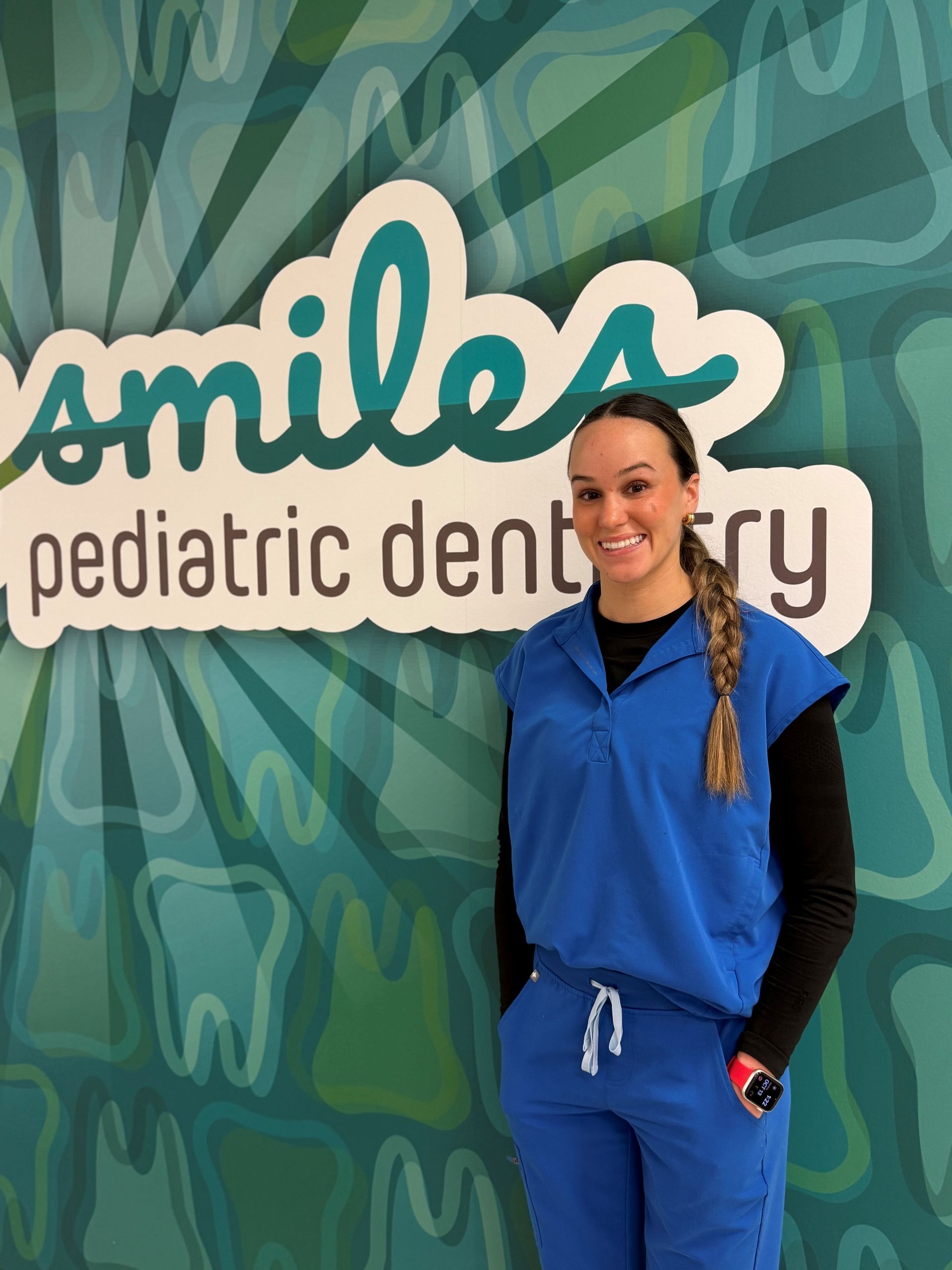 Woman in blue scrubs stands in front of a 