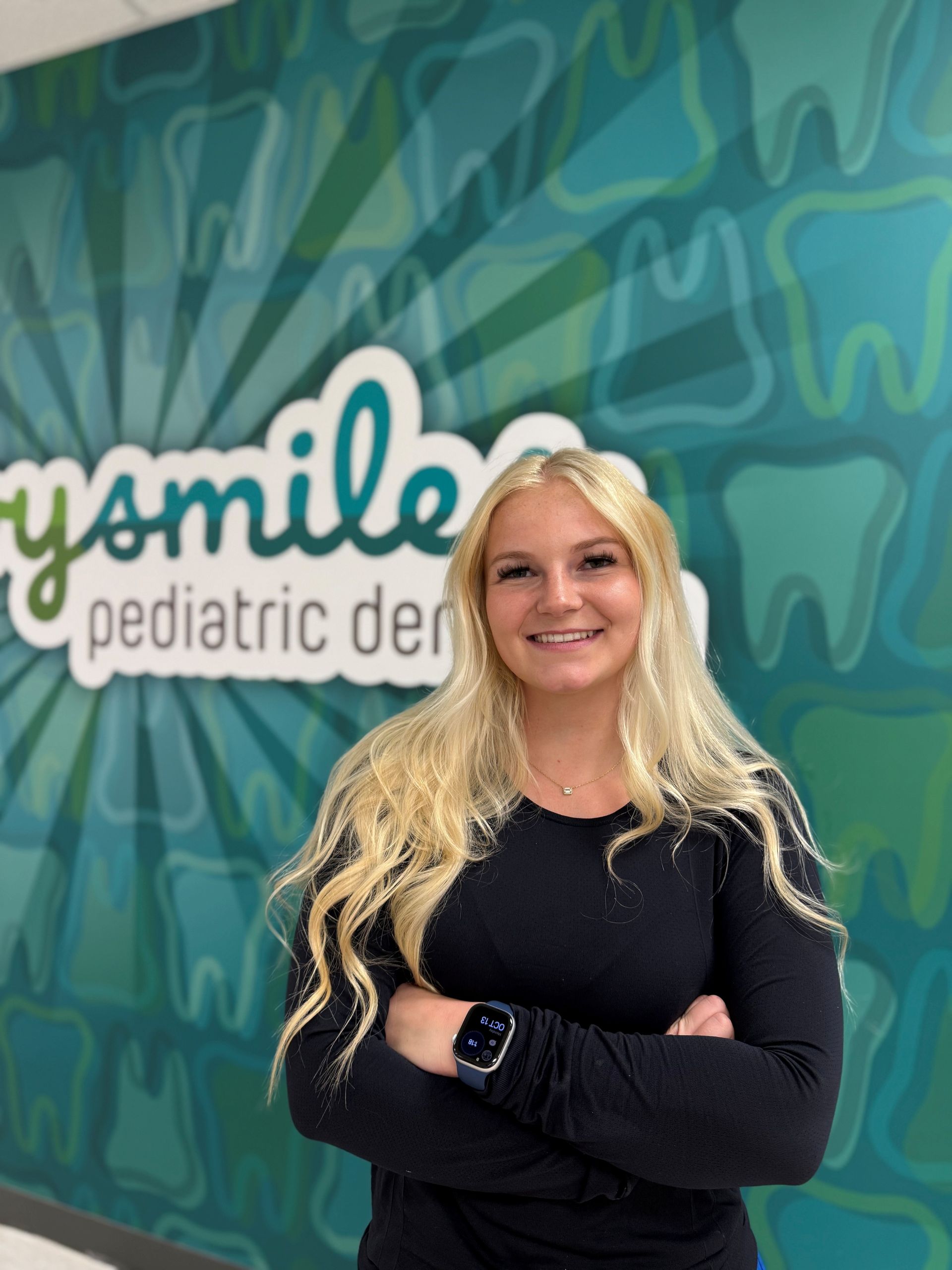 Woman with blonde hair, arms crossed, smiling in front of 