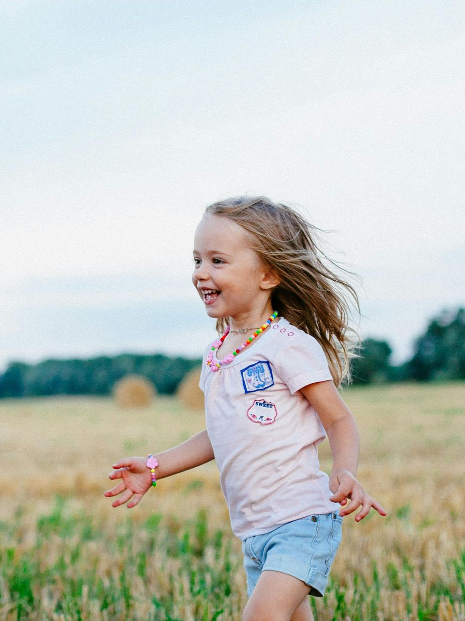 Girl running happily through a harvested field with hay bales in the background.