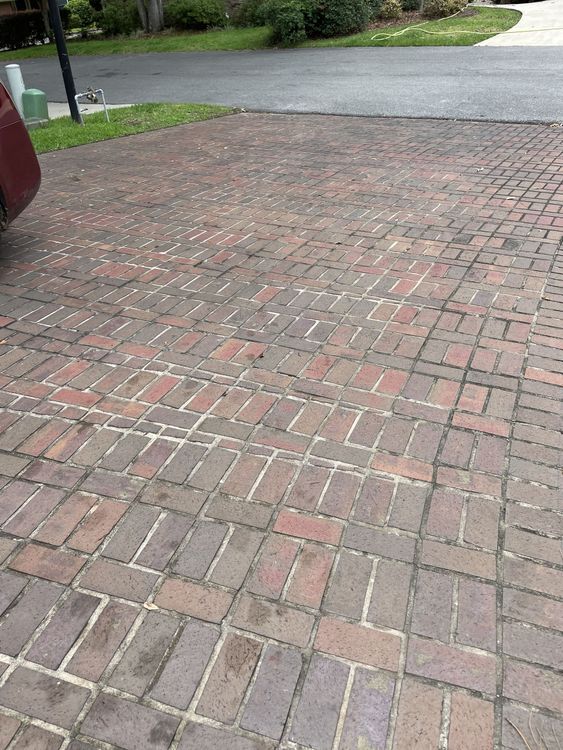 A red car is parked on a brick driveway.