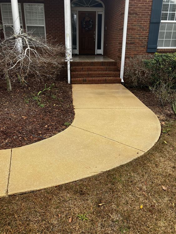 A concrete walkway leading to the front door of a brick house.