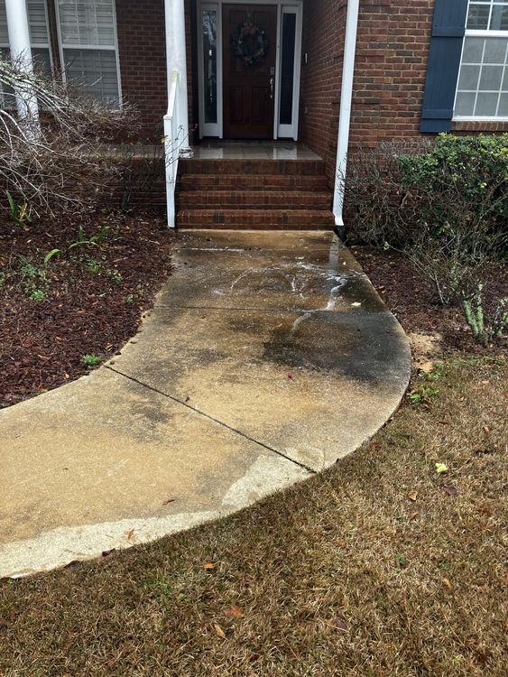 A dirty concrete walkway leading to the front door of a brick house.