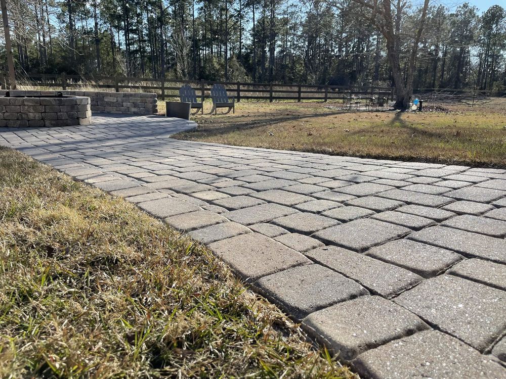 A brick walkway going through a grassy field with a fence in the background.