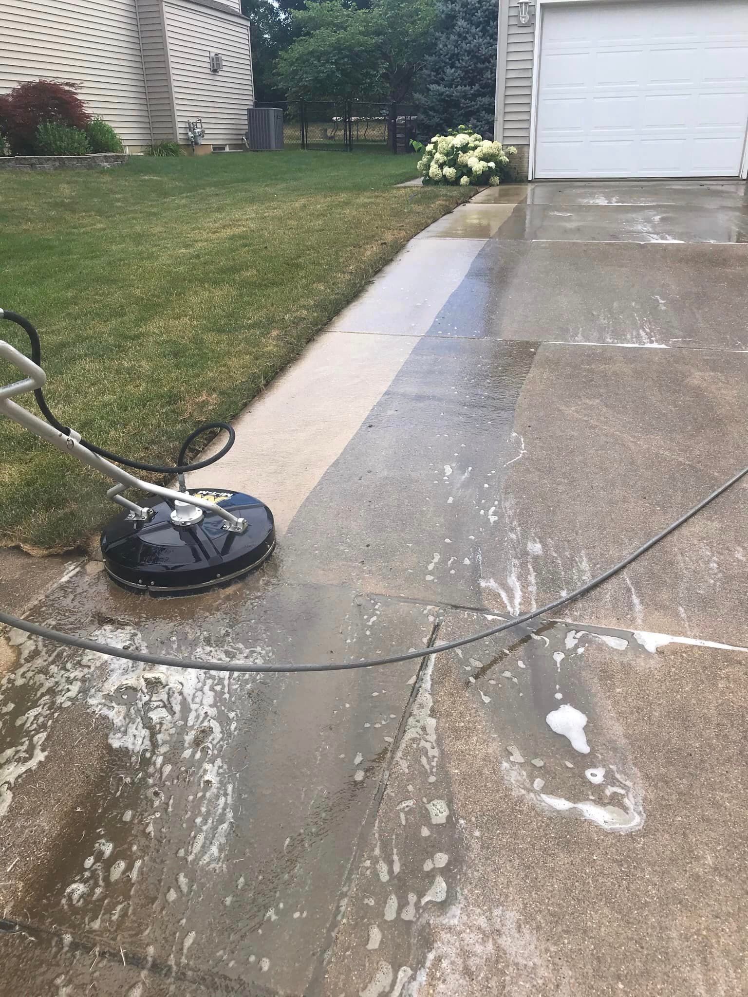 A concrete driveway is being cleaned with a pressure washer.