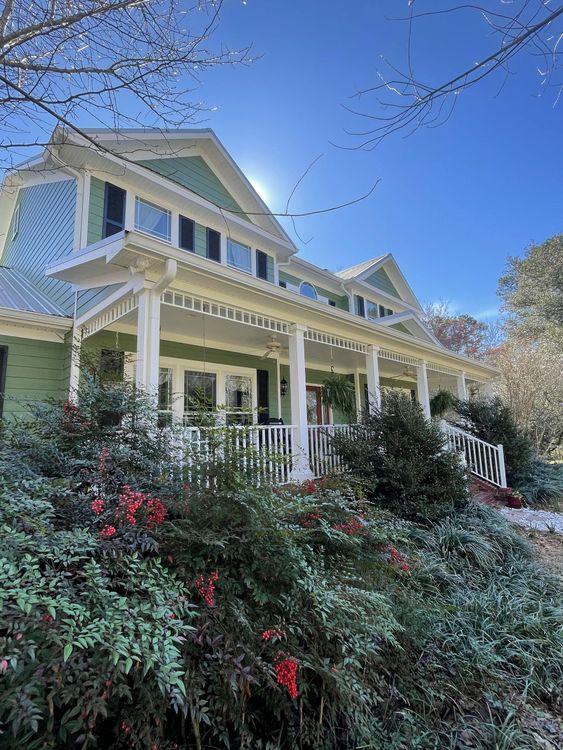 A green house with a white porch and a blue sky in the background