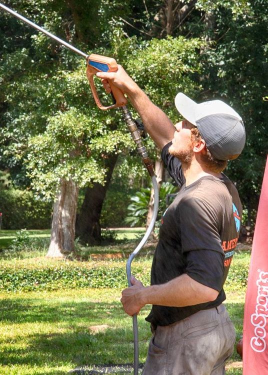 A man in a baseball cap is holding a hose in a park.