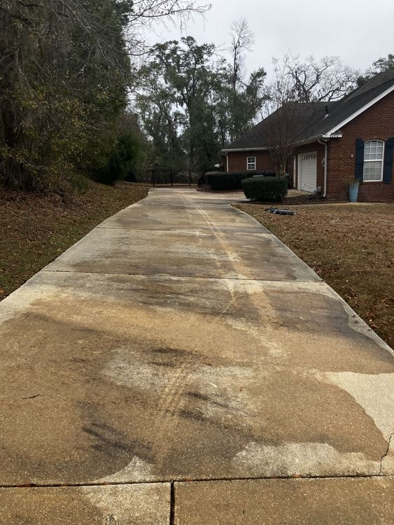 A dirty concrete driveway leading to a brick house.