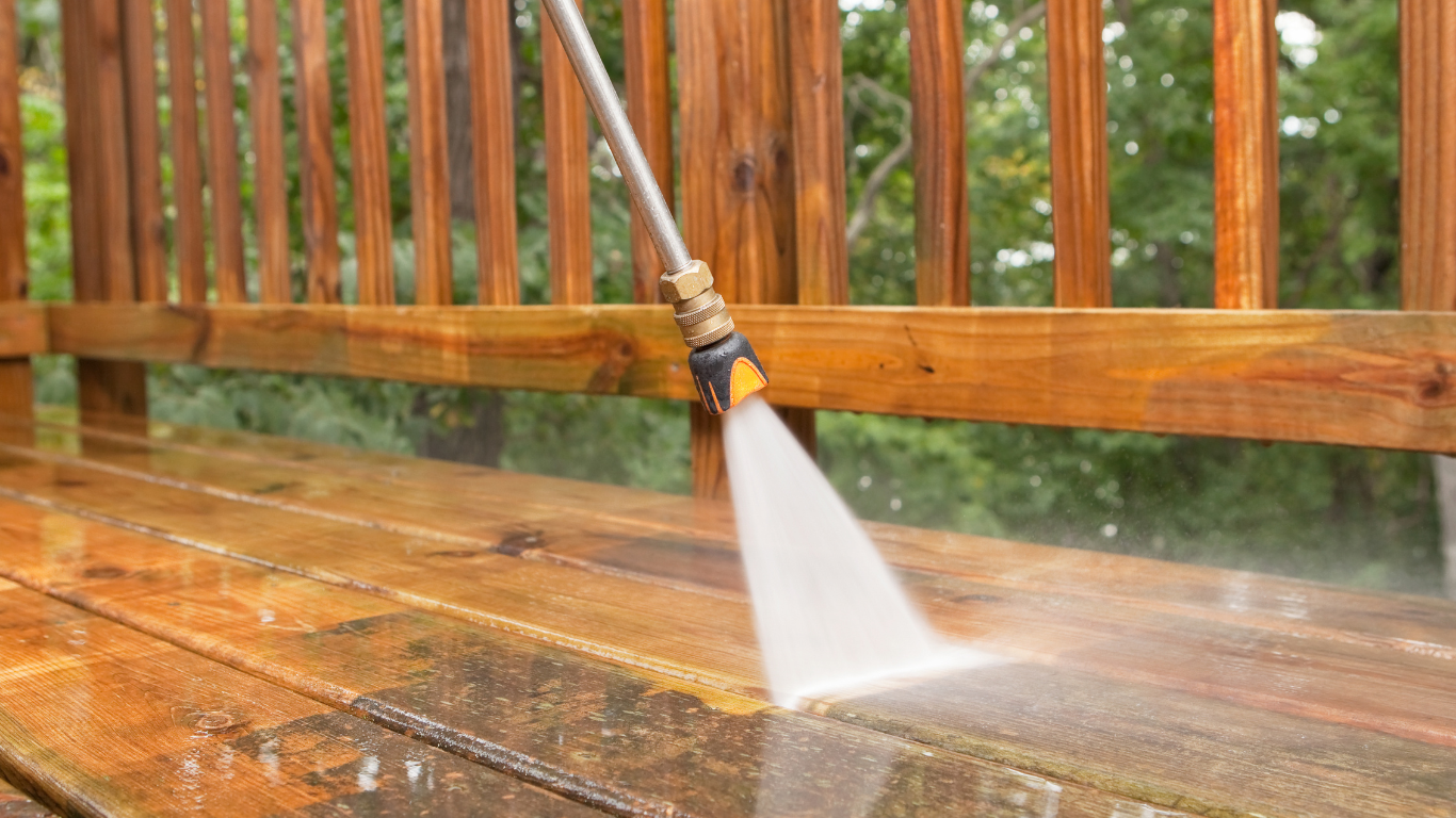 A person is using a high pressure washer to clean a wooden deck.