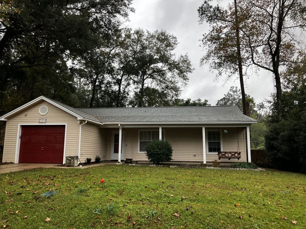 A house with a red garage door and a porch surrounded by trees.