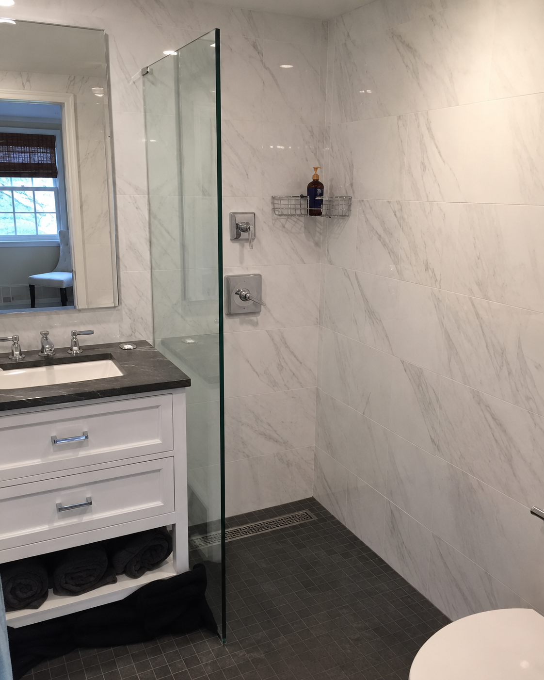 Modern bathroom with marble walls, glass shower panel, dark tile floor, and white vanity sink.