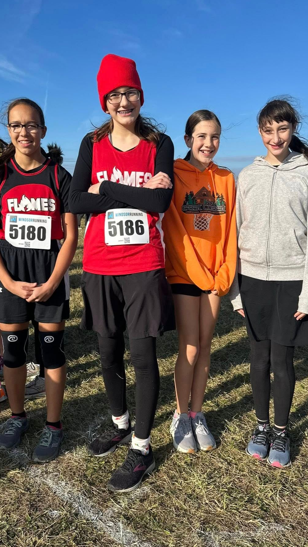A person wearing a hat and orange shirt, holding a baseball bat on their shoulder on a baseball field.