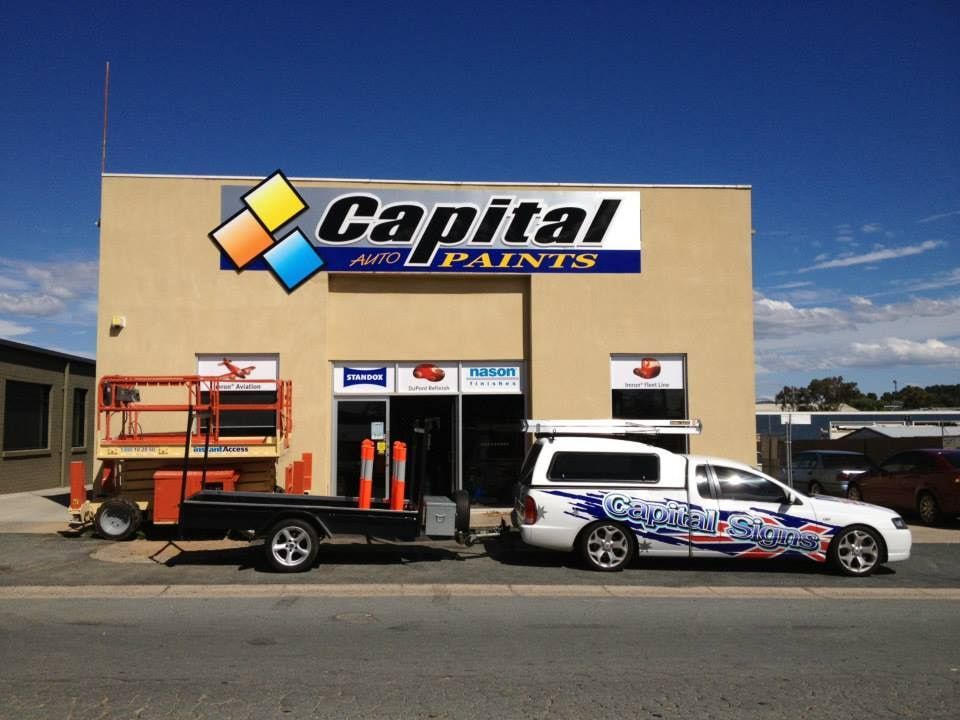 Two Cars Are Parked In Front Of A Building That Says Capital Paints — Capital Signs in Canberra, ACT