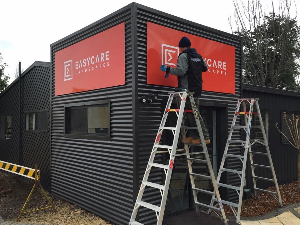 A Man On A Ladder Is Installing A Sign On The Side Of A Building — Capital Signs in Fyshwick, ACT