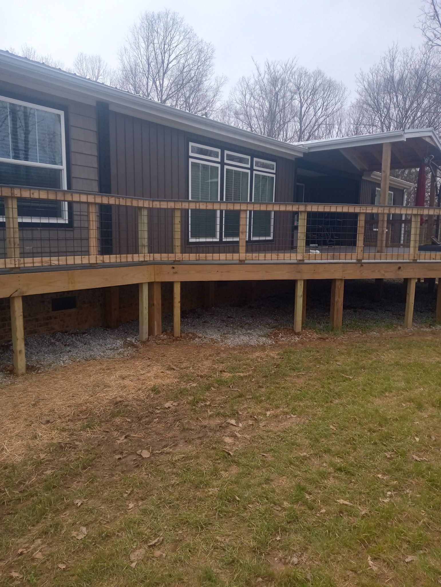 Brown house with a wooden deck in a grassy yard.