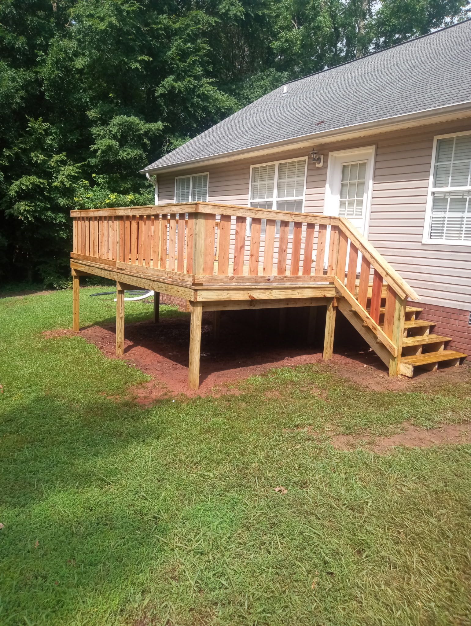 A wooden deck with stairs attached to the side of a house. Green grass surrounds the deck.