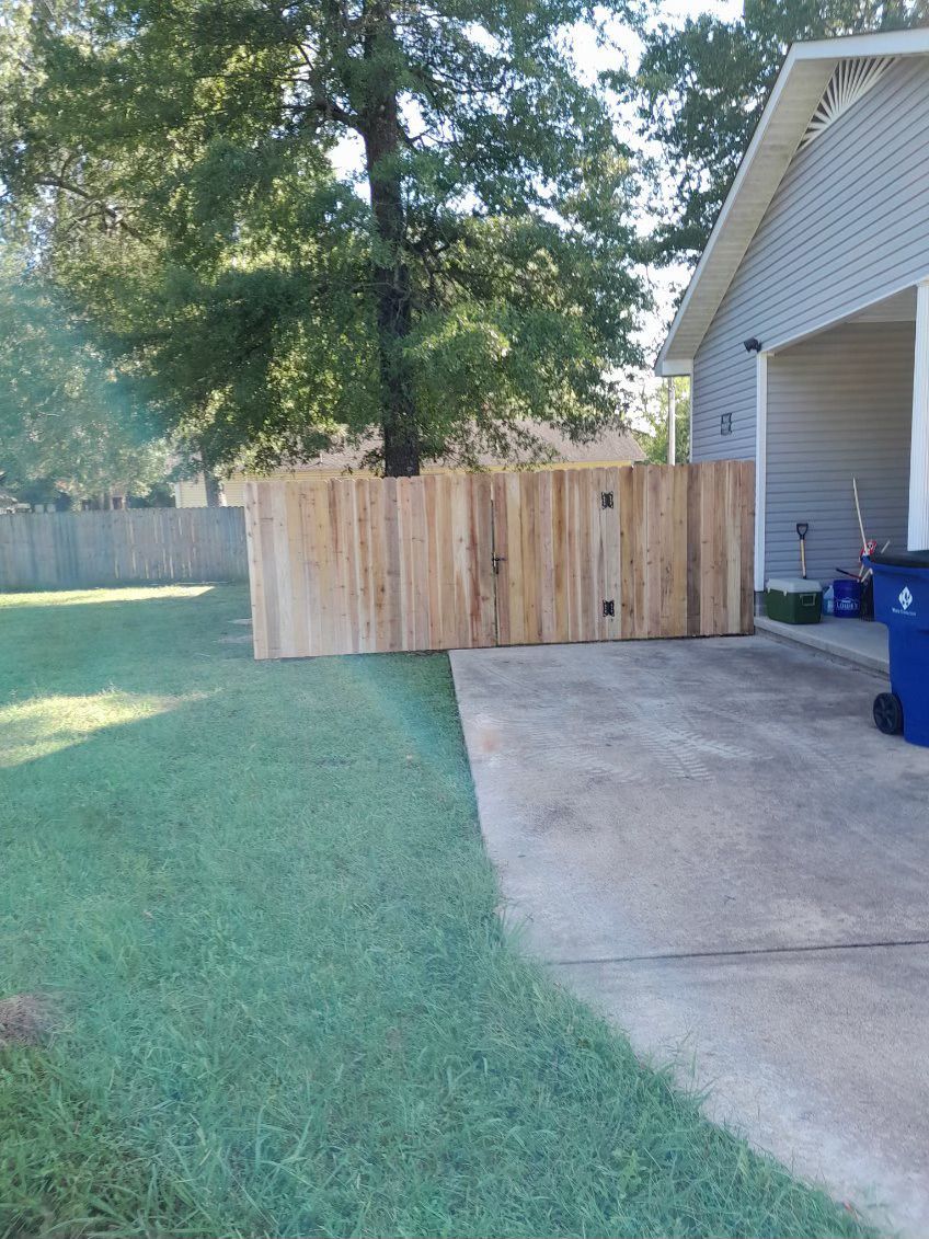 Wooden fence in a backyard next to a house, green grass and a tree.