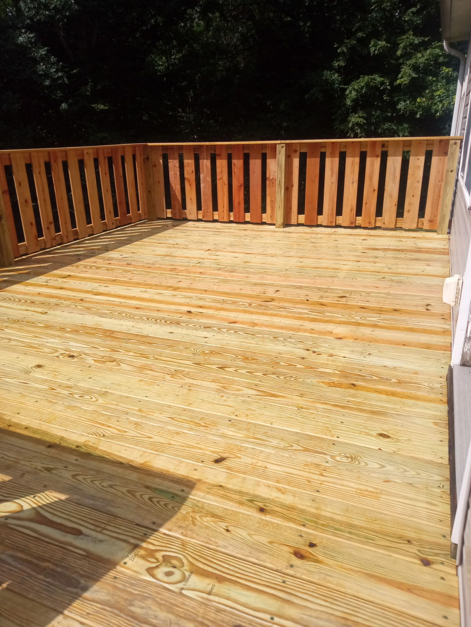 Wooden deck with railing, surrounded by trees.