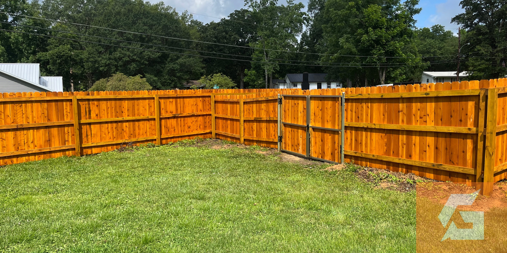 Wooden fence surrounds a grassy yard. Trees and a cloudy sky are in the background.