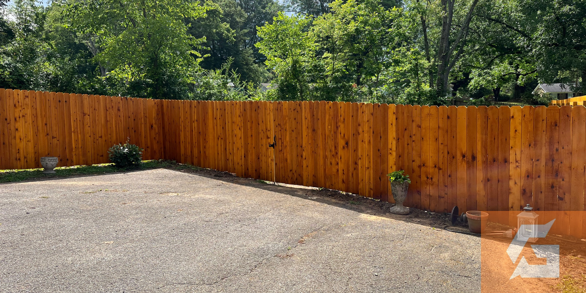 Brown wooden fence with gravel ground in front; trees behind.