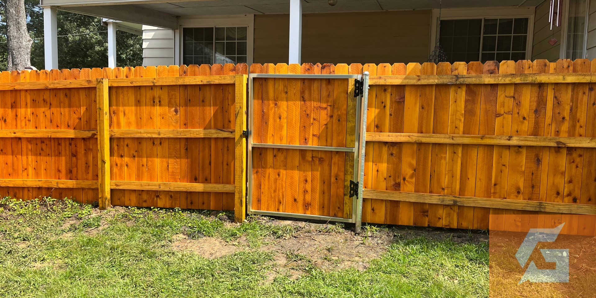 A wooden fence with a gate in a yard. The fence is stained a warm orange, with green grass below.