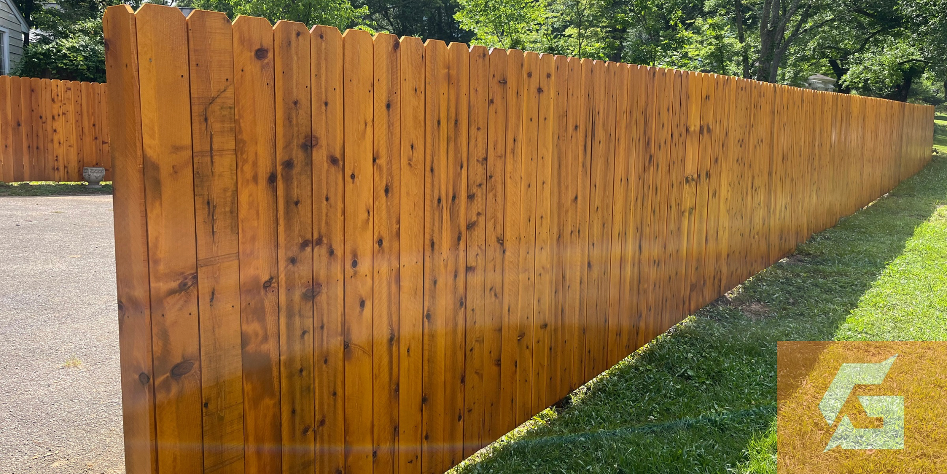 Wooden fence stained a warm brown, stretches along a green lawn on a sunny day.