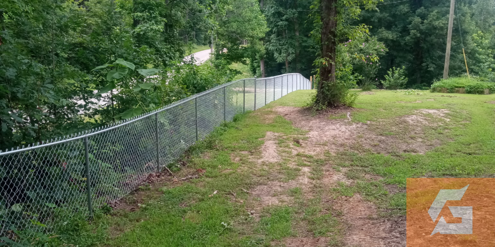 Chain-link fence borders a grassy area near trees, overcast sky.