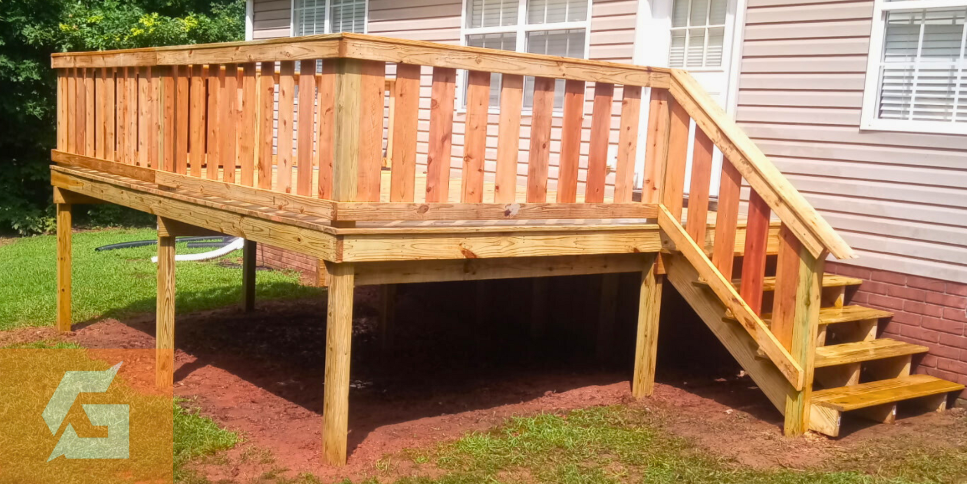 Wooden deck with stairs and railing, attached to a light-colored house, set on red mulch.