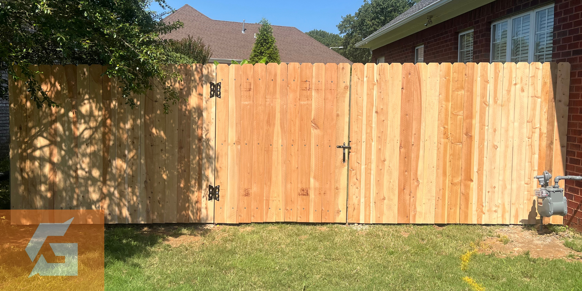 A wooden fence with two gates, in front of grass, a house, and a blue sky.