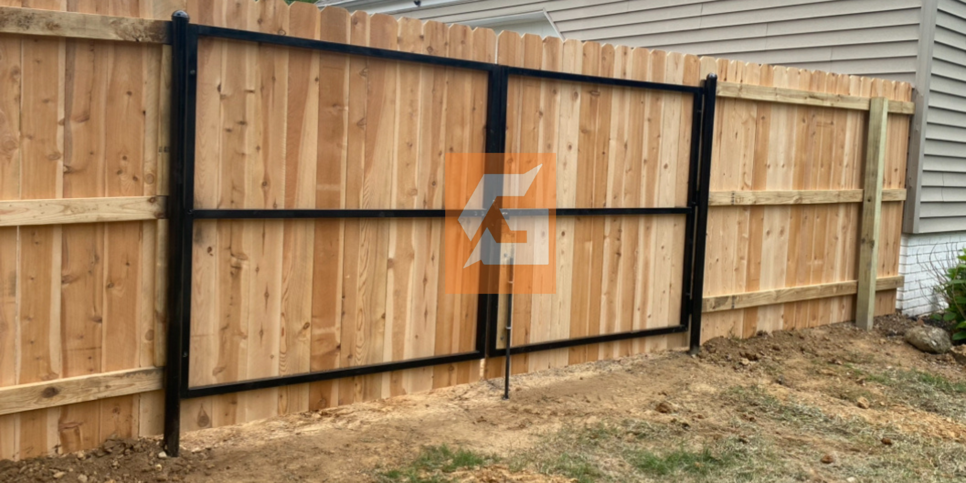 Black metal gate installed in a wooden fence, grassy yard, and a house in the background.