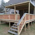 Wooden deck with stairs leading up to a covered area, attached to a house.