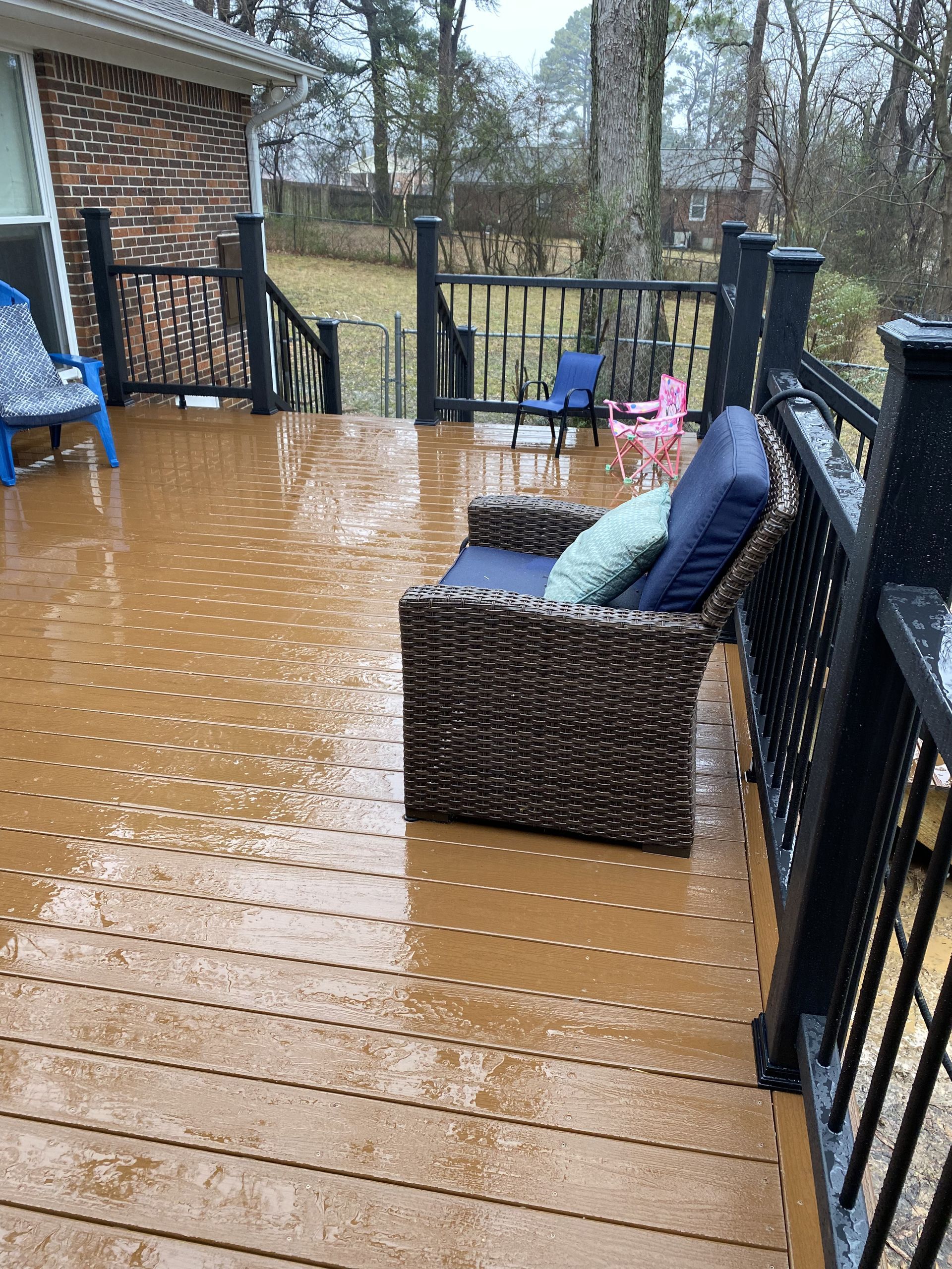 A wet, brown deck with a wicker couch and railing. Rain and snow in an outdoor setting.