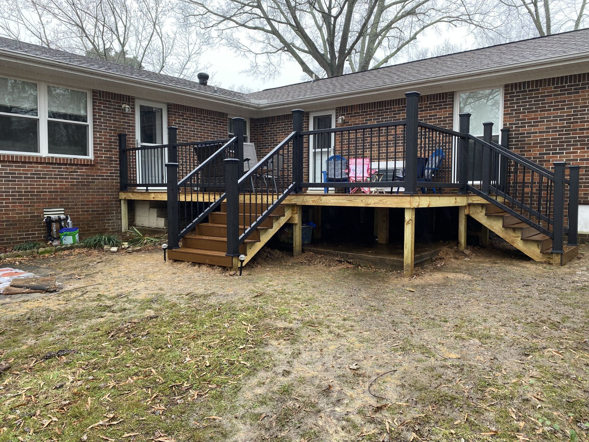 Backyard deck with black railing, wood steps, and brick house exterior.